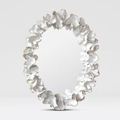 a circular mirror with white flowers on it's sides and an oval frame in the middle