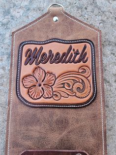 a brown leather case with the word meredith on it and a flower design