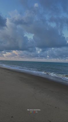 a person walking on the beach with a surfboard in their hand under a cloudy sky