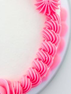 a white cake with pink icing on top and flowers in the middle, sitting on a plate