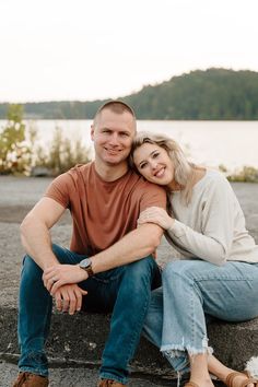 a man and woman sitting next to each other in front of a body of water