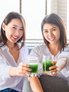 two women sitting on a couch holding glasses of green juice