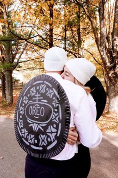 two people hug each other while holding an oreo cookie in front of trees and leaves