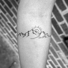 a person with a tattoo on their arm that has mountains in the background and sun above them