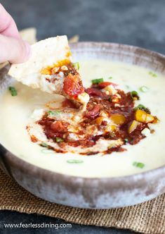 a hand dipping a tortilla chip into a bowl of soup