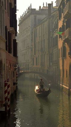 a man in a gondola on a narrow canal with buildings lining both sides