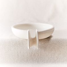 a white bowl with two handles sitting on top of a cloth covered tableclothed surface