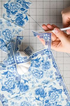 someone is cutting out blue and white paper with scissors on a piece of cloth that has been cut into smaller pieces