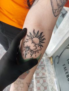 a person with a tattoo on their arm is holding onto a black glove that has the sun and cloud tattooed on it