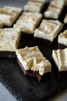 several pieces of brownie with white frosting sitting on a black tray next to each other