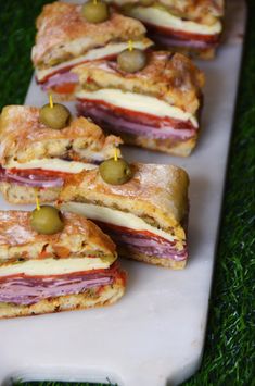 several sandwiches with meat, cheese and olives on a white platter in the grass