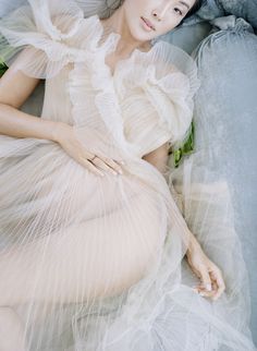 a woman laying on top of a blue couch wearing a white dress and large hat