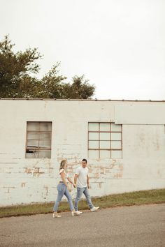 a man and woman walking down the street in front of an old white brick building