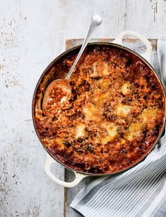 a pot filled with pasta and sauce on top of a wooden table next to a spoon