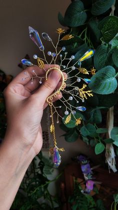 a person holding a piece of jewelry in front of a green plant with leaves on it