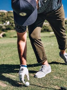 a man with his foot on the ground wearing a baseball cap and holding a golf club