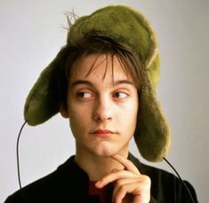 a young man wearing a green hat with ear buds in his ears and looking at the camera