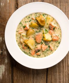 a white bowl filled with potato and salmon chowee on top of a wooden table