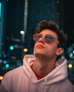 a young man wearing sunglasses looking up at the sky in front of some buildings and lights