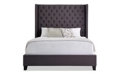 an upholstered bed with white sheets and gray headboard, pillows and throw pillows