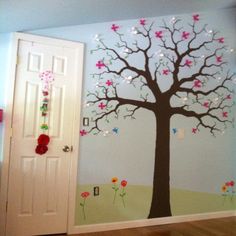 a room with a tree painted on the wall next to a white door and wooden floor