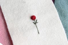 a single red rose sitting on top of a white piece of felt next to another piece of fabric