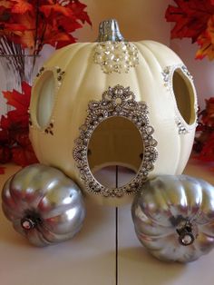 a white pumpkin shaped like a carriage with jewels on the front and sides, sitting in front of fall leaves