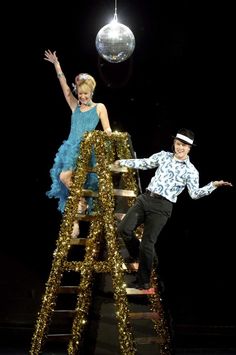 a man and woman are standing on a ladder in front of a disco ball,