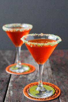 two cocktail glasses filled with red liquid on top of a wooden table