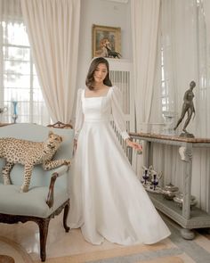 a woman in a white wedding dress standing next to a cheetah on a couch