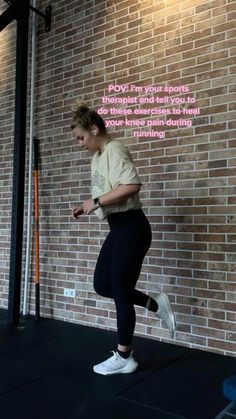 a woman in black pants and white sneakers is doing exercises on the floor with a brick wall behind her