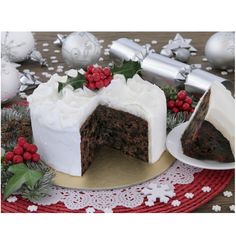 a chocolate cake with white frosting and holly decorations on a red doily next to silver baubles