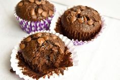 three chocolate muffins sitting on top of a white table cloth covered in chocolate chips