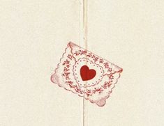 a red and white doily with a heart hanging from it's side on a wall