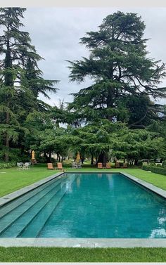 an empty pool in the middle of a lush green yard with trees and lawn chairs