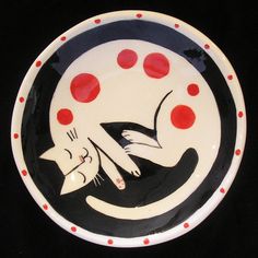 a black and white plate with red polka dots on the rim that has a cat in it