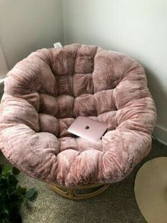 a pink chair with a laptop on it sitting in front of a wall and potted plant