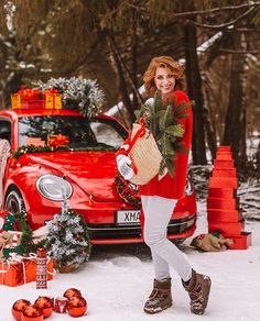 a woman is walking in the snow with her christmas tree and gift bags next to a red car