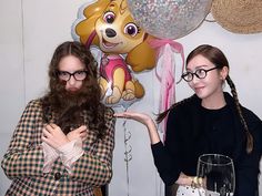 two women standing next to each other in front of balloons and balloon animals on the wall