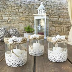 three glass jars with lace and bows on them sitting on a wooden table next to a lantern