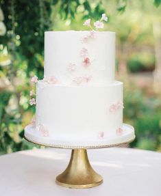 a white wedding cake with pink flowers on it sitting on top of a gold plate