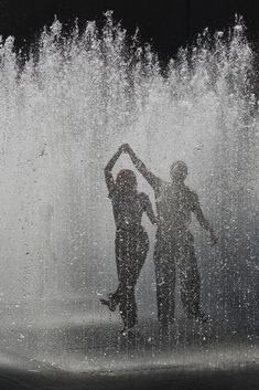 two people standing in front of a fountain with water spouting all around them