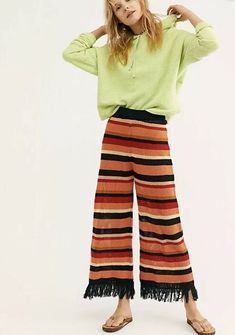 a woman standing in front of a white background wearing striped pants and a green sweater