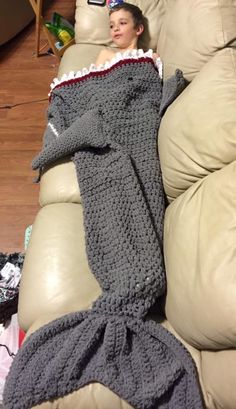 a young boy laying on top of a couch covered in a crocheted blanket