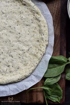 a pizza dough sitting on top of a wooden cutting board next to spinach leaves