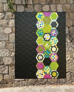 a quilted wall hanging on the side of a brick building next to a stone wall