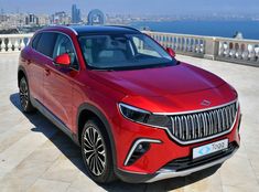 a red suv parked on the side of a road in front of a body of water