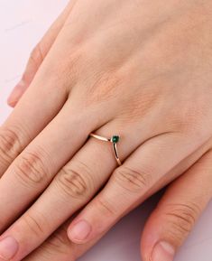 a woman's hand wearing a gold ring with a green stone on it and a diamond in the middle