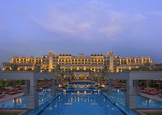 an outdoor swimming pool in front of a large building at dusk with lit up lights