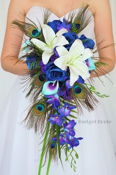 the bride is holding her blue and white bouquet with peacock feathers on it's side